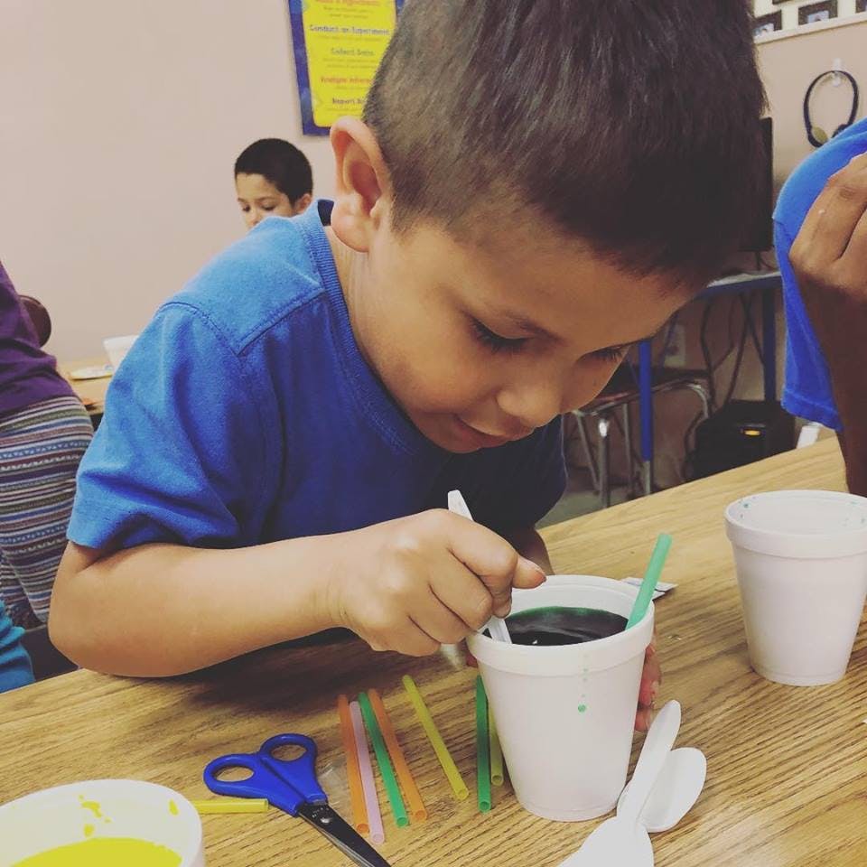 Child stirring liquid in a cup with a spoon