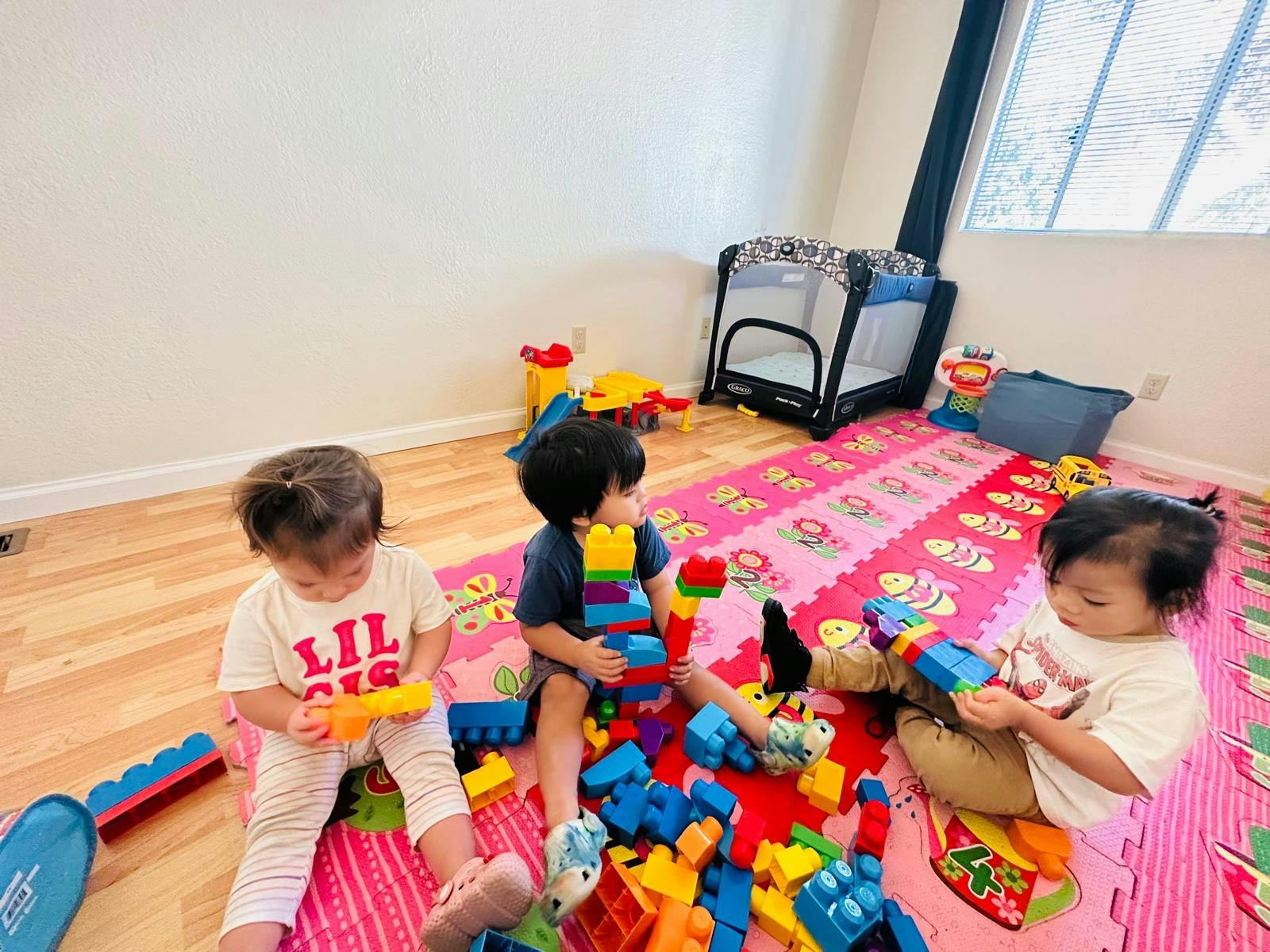 Three children playing with colorful building blocks on a pink mat