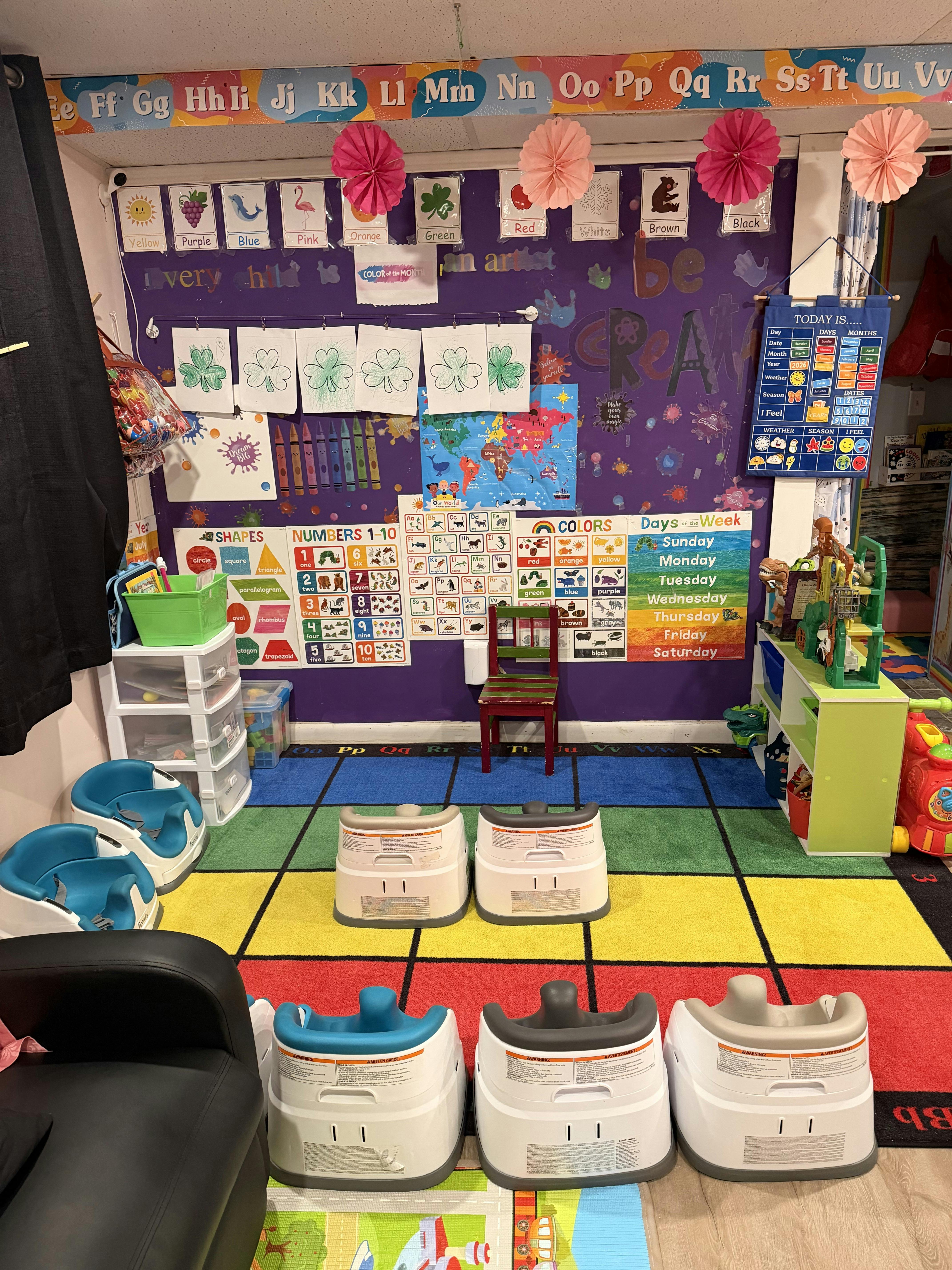 Classroom with colorful rug, learning posters on wall, and booster seats on the floor