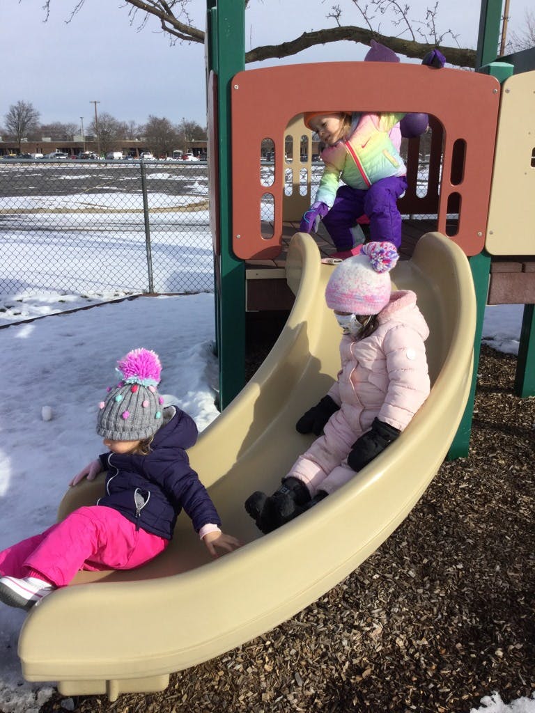 Three children playing on a slide in a snowy playground