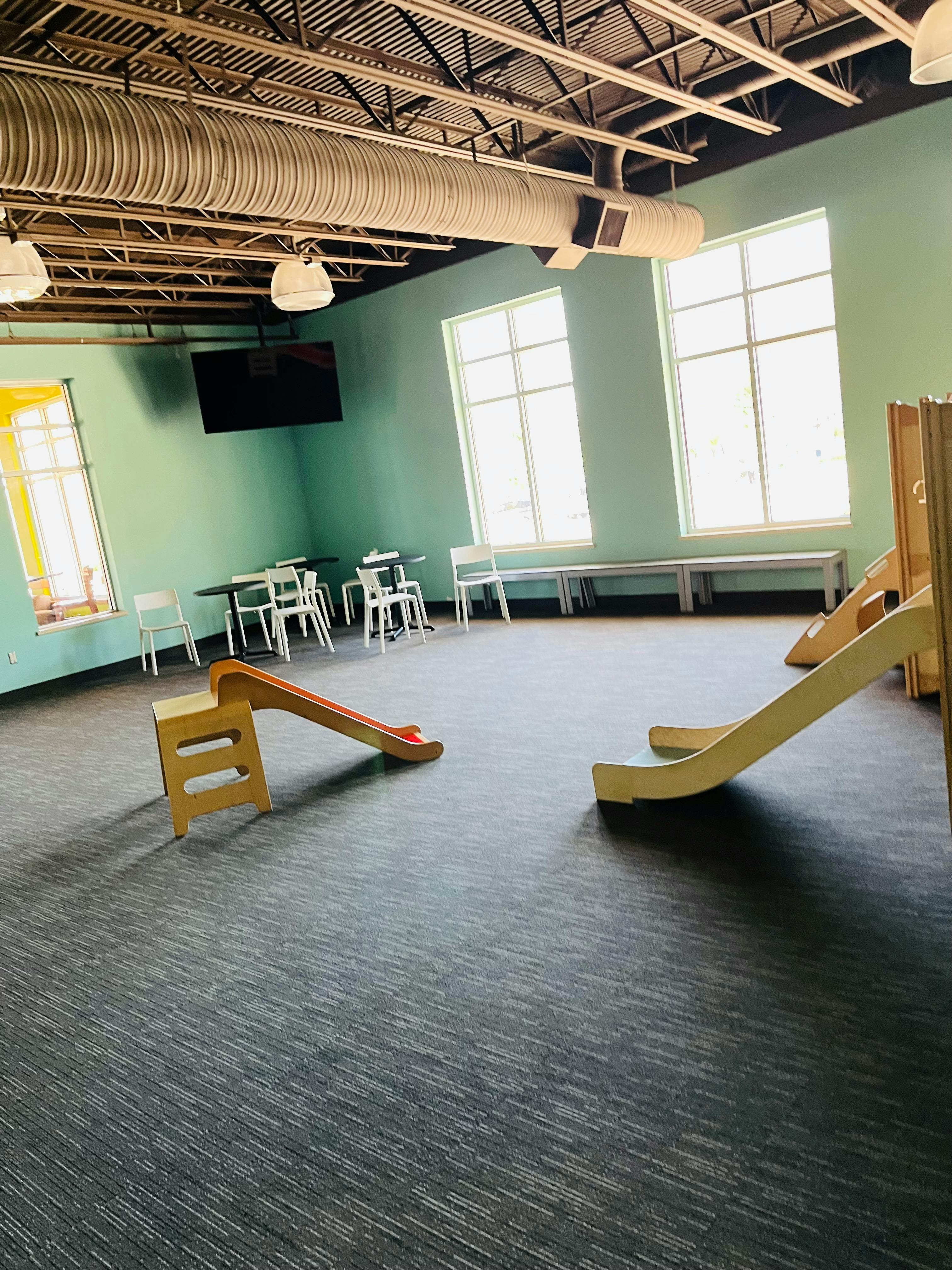 Two small wooden slides on a carpeted floor in a room with large windows