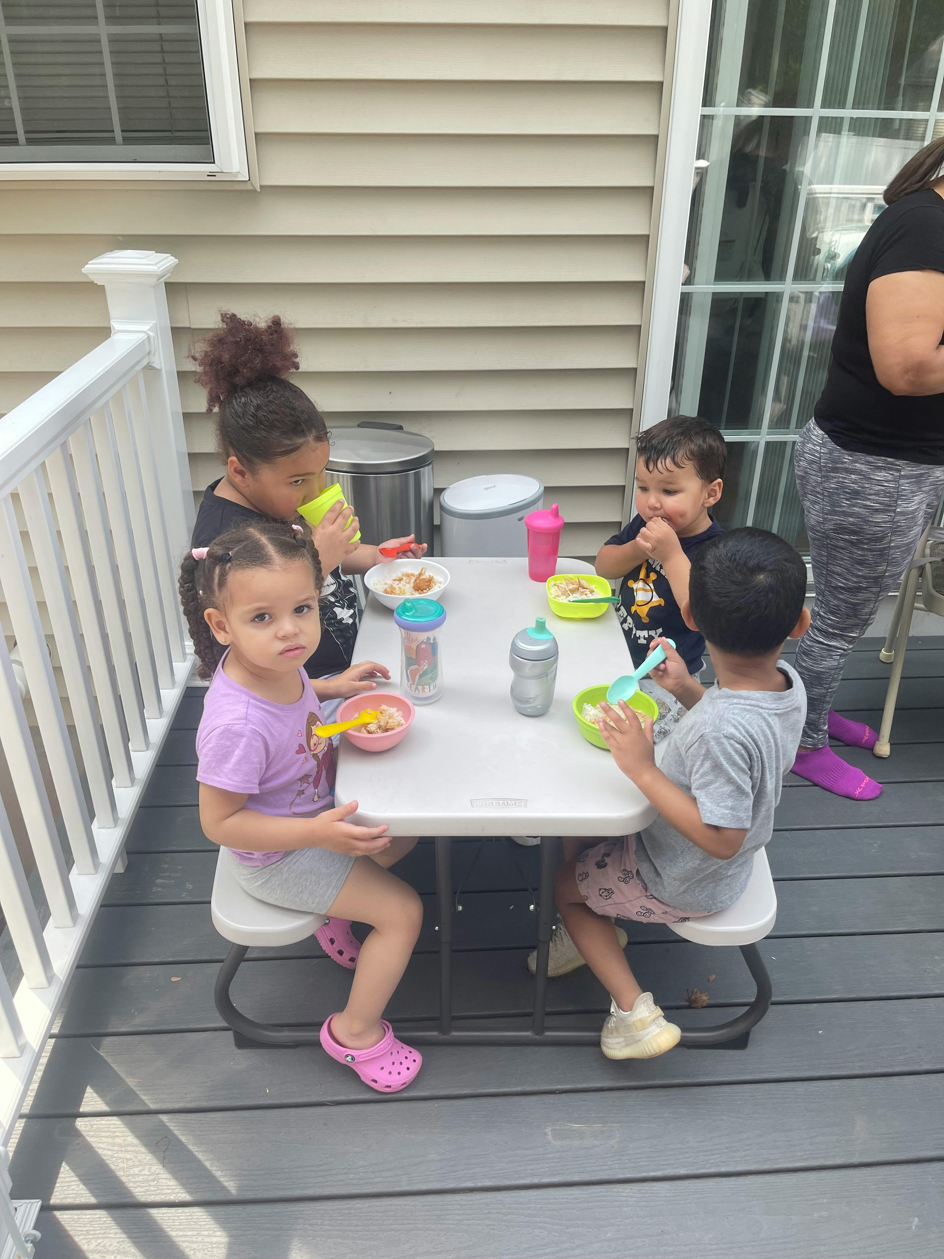 Four children eating at a small table outdoors