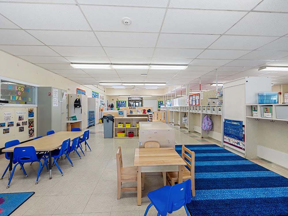 Classroom with child-sized tables and chairs, cubbies, and a blue striped rug