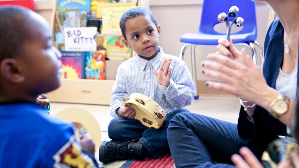 Child holding a tambourine and looking at a person clapping