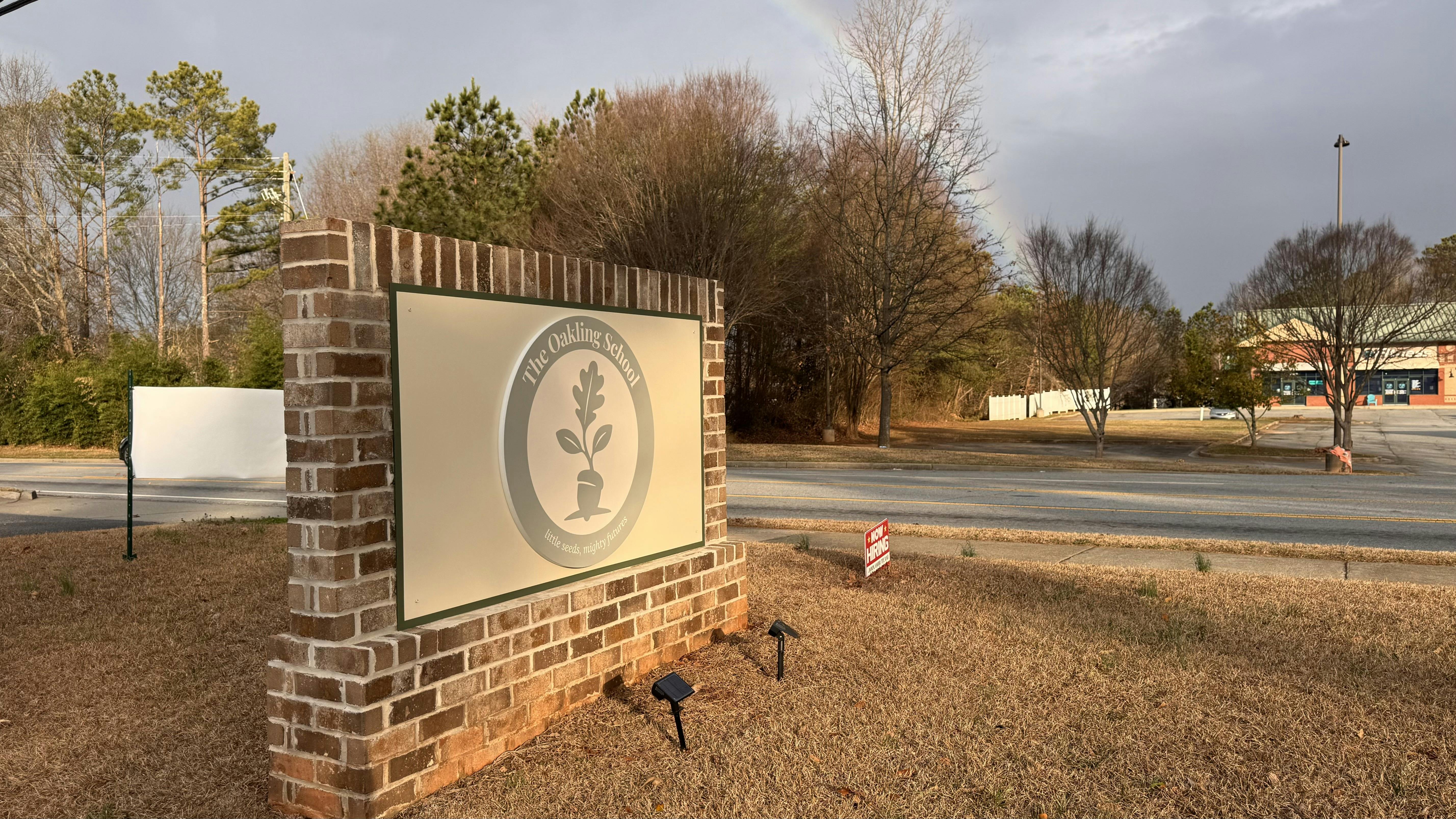 Brick sign for The Oakling School with a plant logo, a street in the background