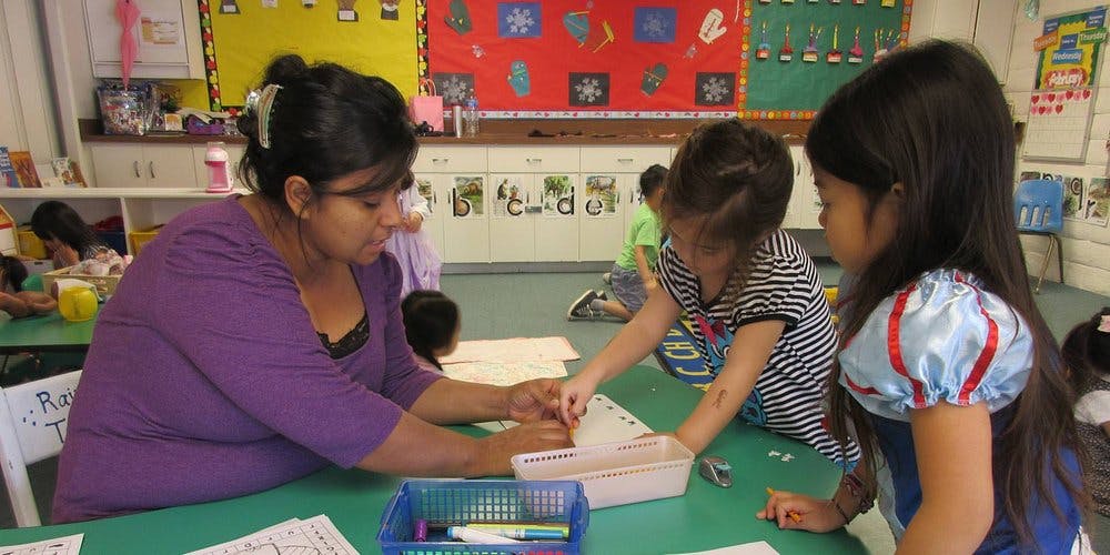 Person and two children working at a table in a classroom