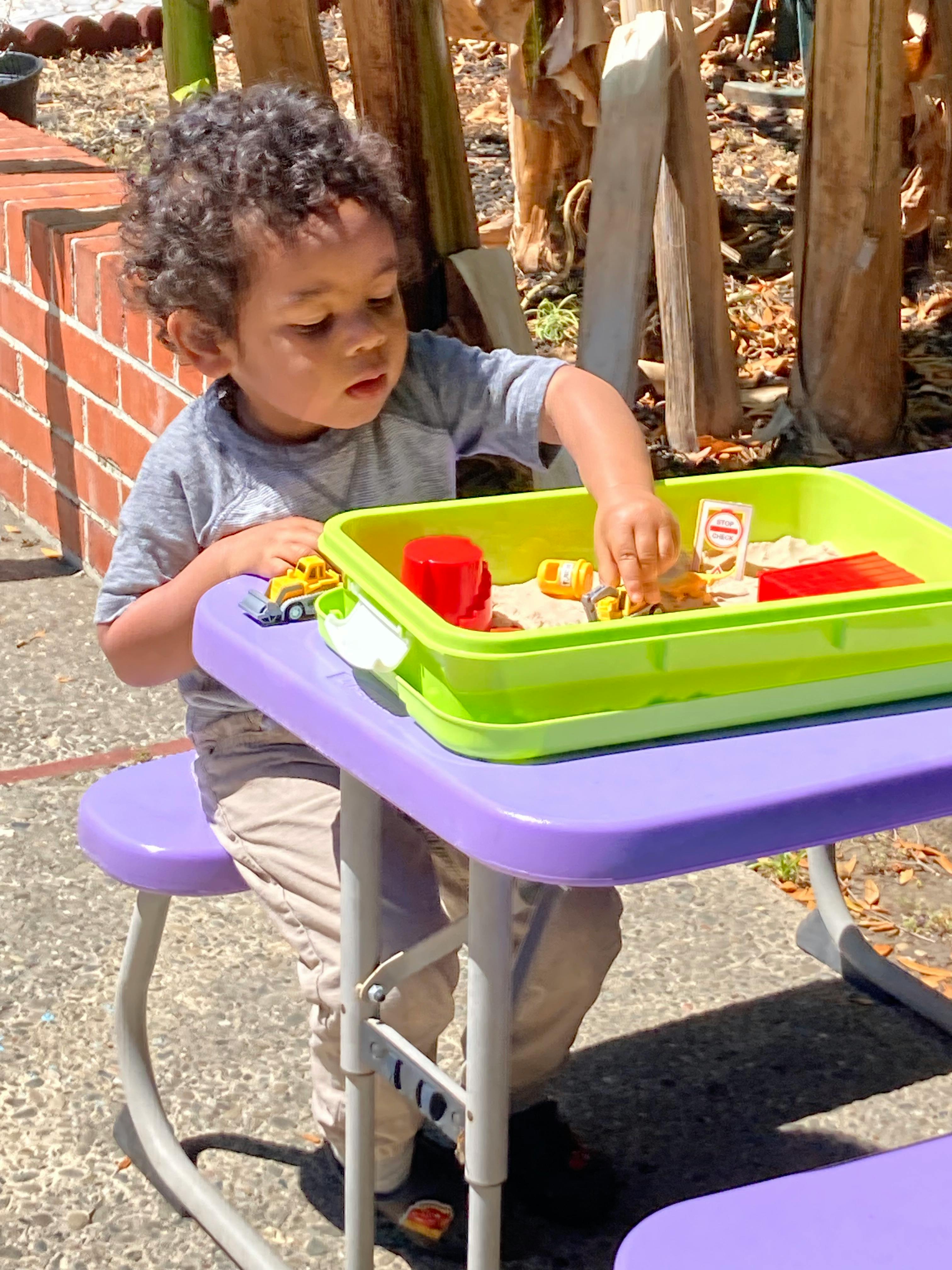 Child playing with toys in a sand tray on a purple table