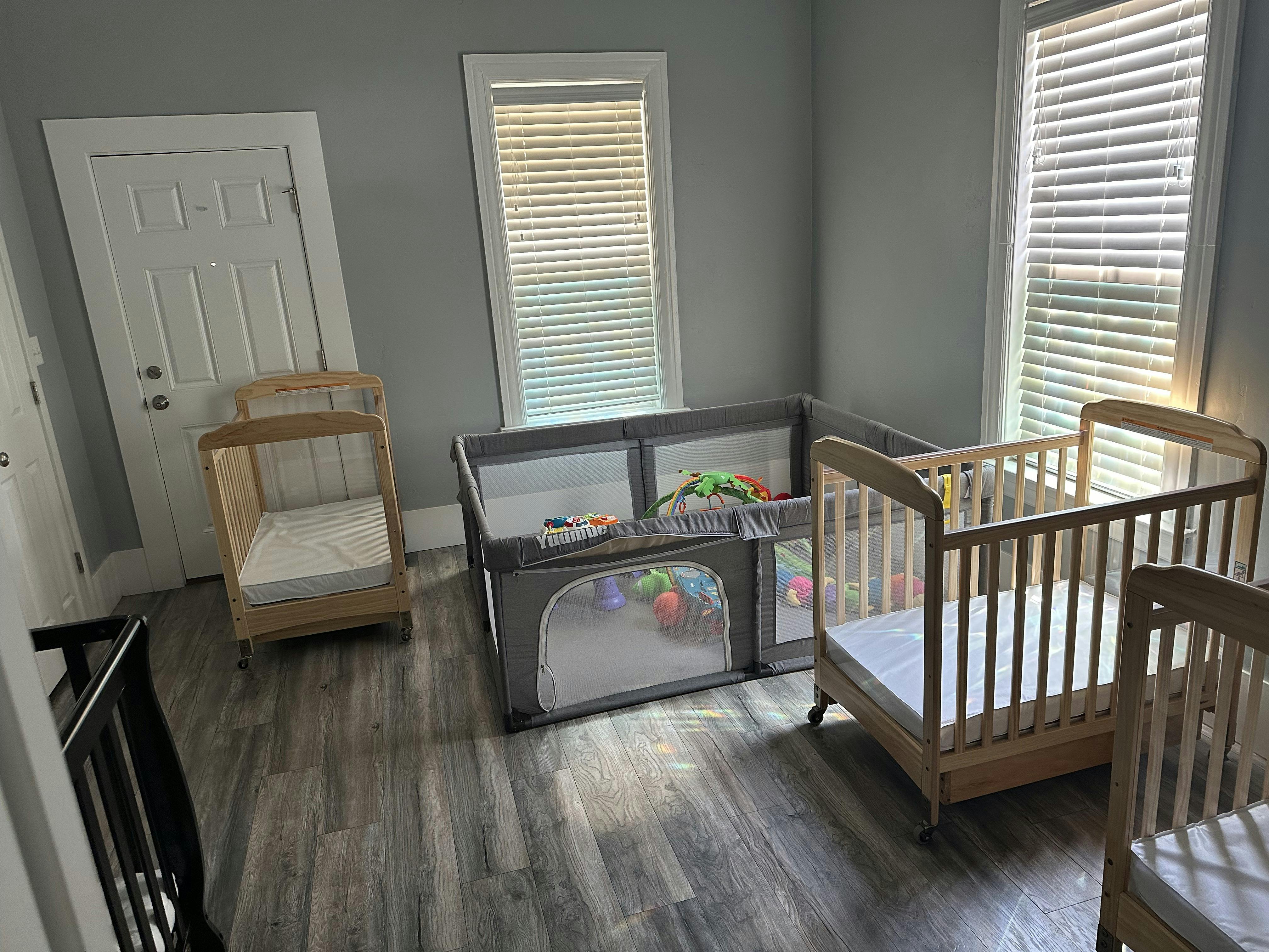 Two wooden cribs and a gray playpen in a room