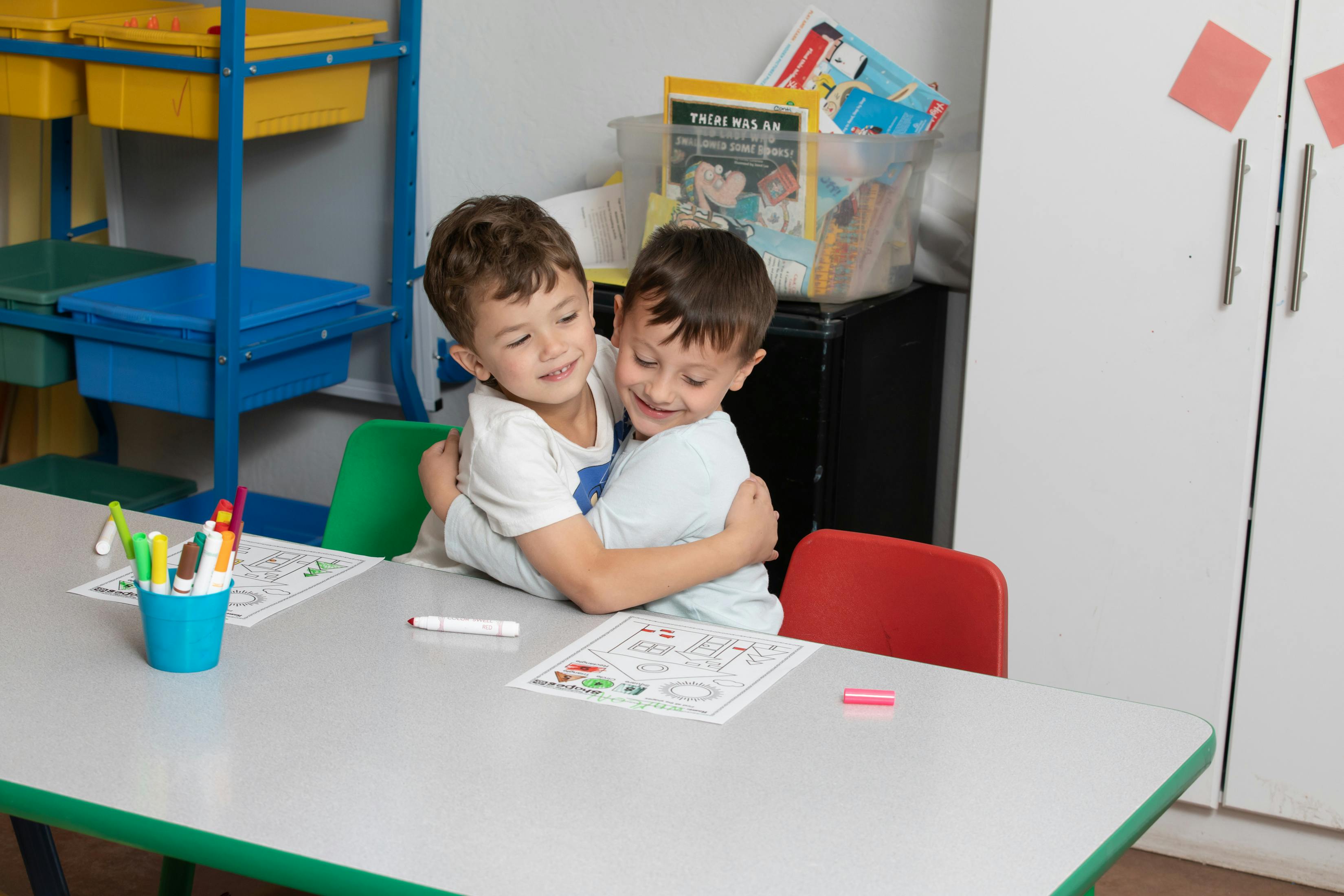 Two children hugging at a classroom table