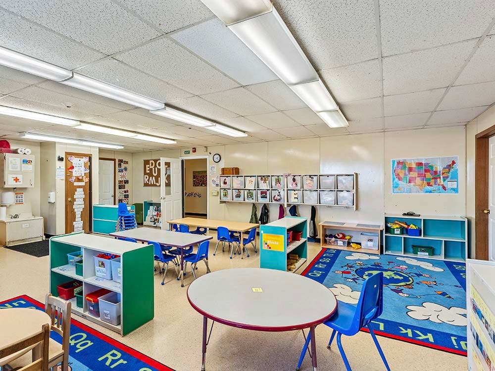Empty classroom with small tables, chairs, and play mats