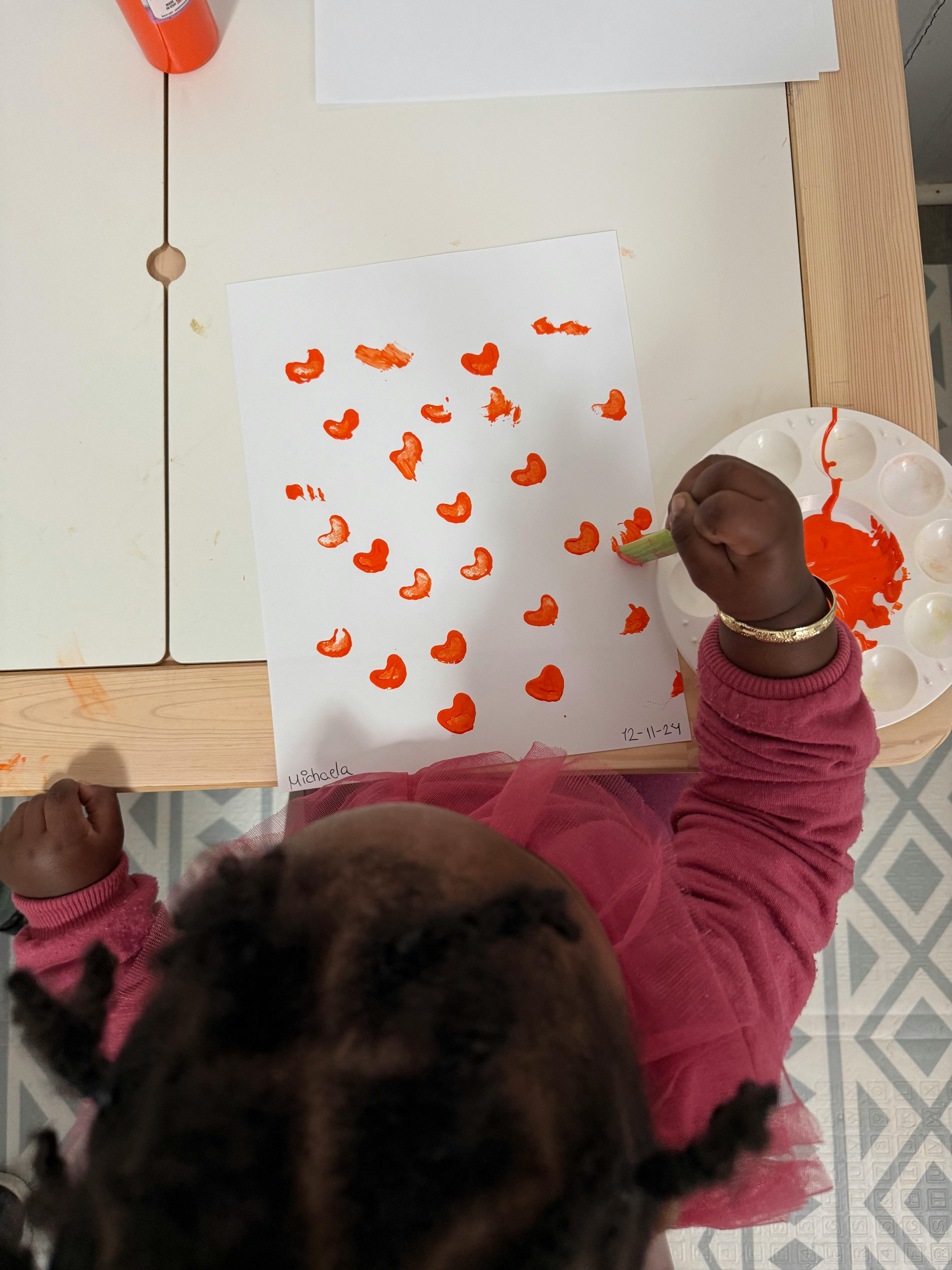 Child painting orange heart shapes on a piece of paper