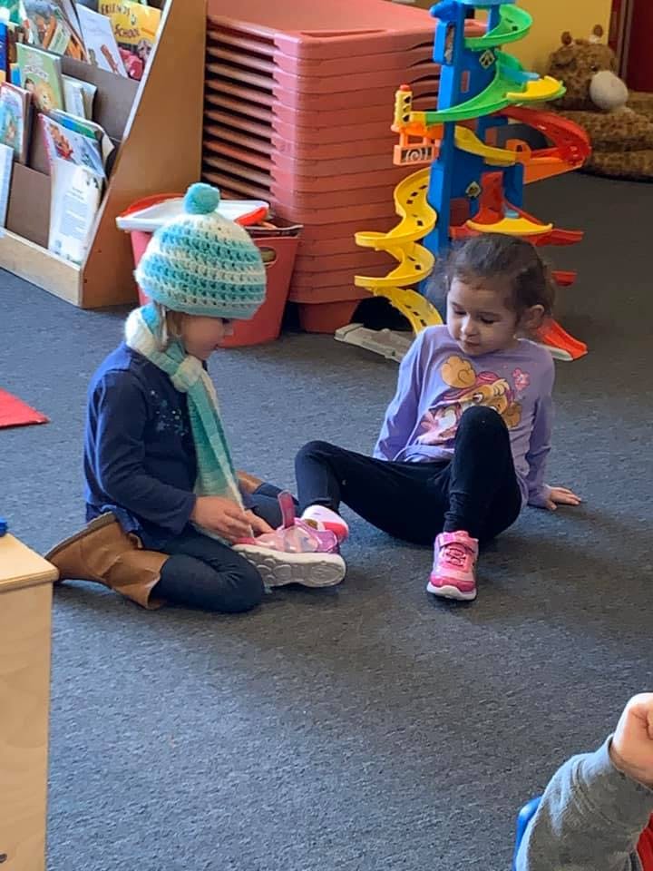 Two children sitting on the floor, one wearing a hat and scarf
