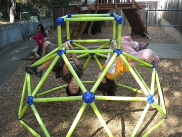 Two children hanging upside down on a jungle gym
