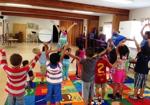 Adults and children with arms raised in a classroom