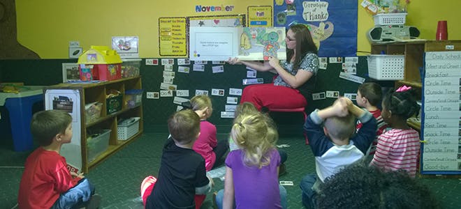 Person reading a book to a group of children in a classroom