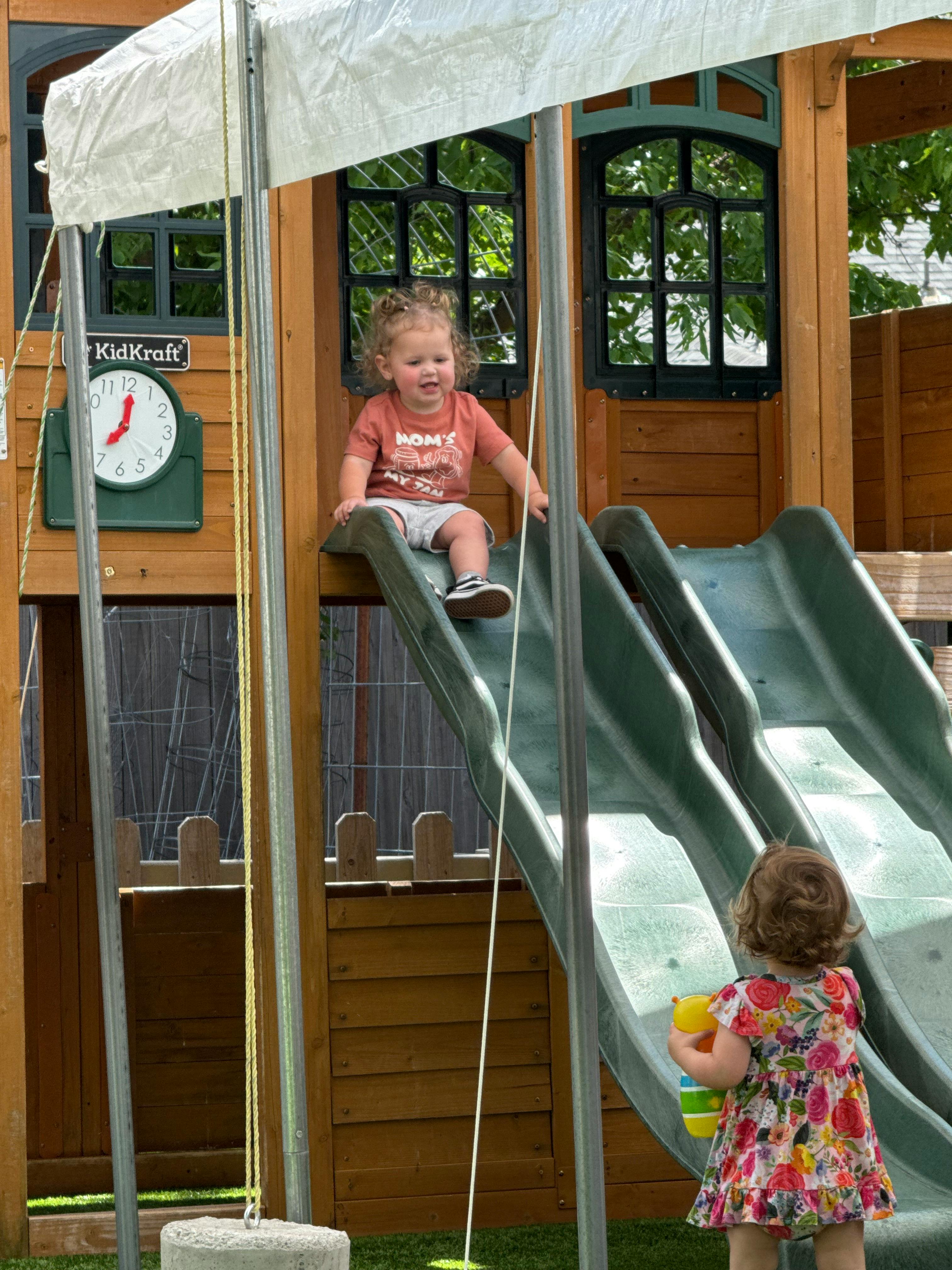 Child sitting at the top of a slide, another child at the bottom