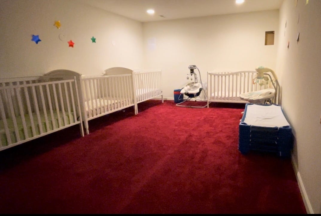 Room with red carpet, multiple white cribs, and a baby swing