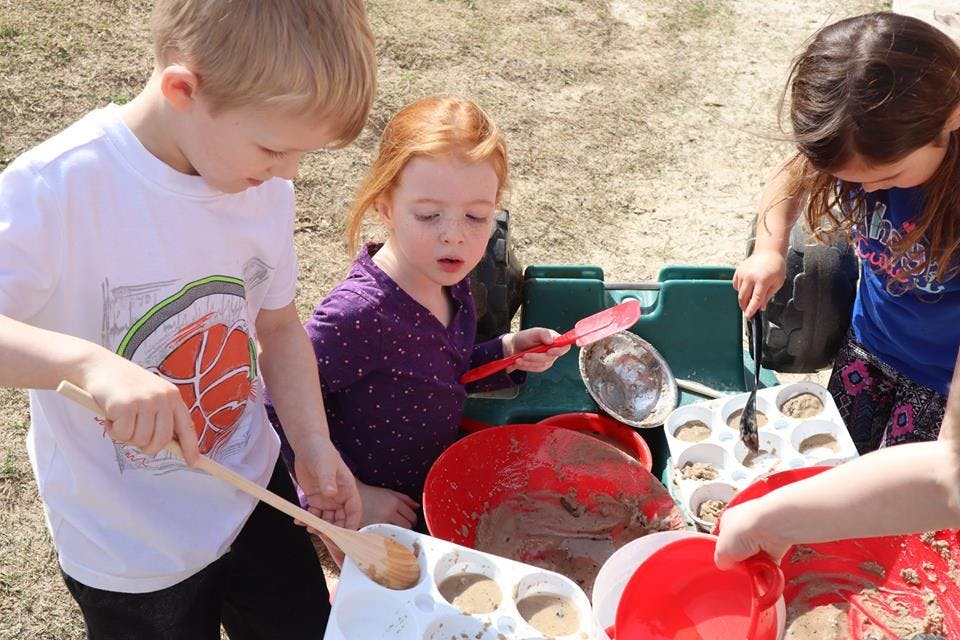 Three children playing with dirt and kitchen toys outdoors