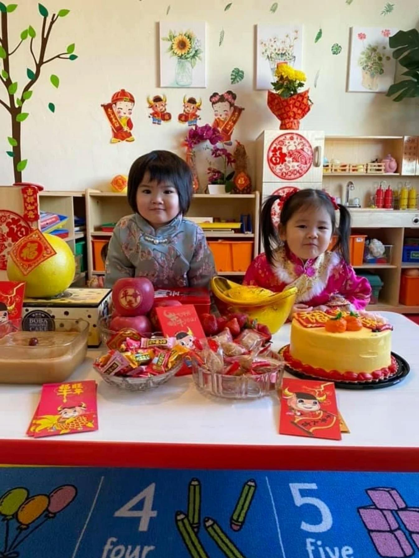 Two children sitting at a table with a cake and other items