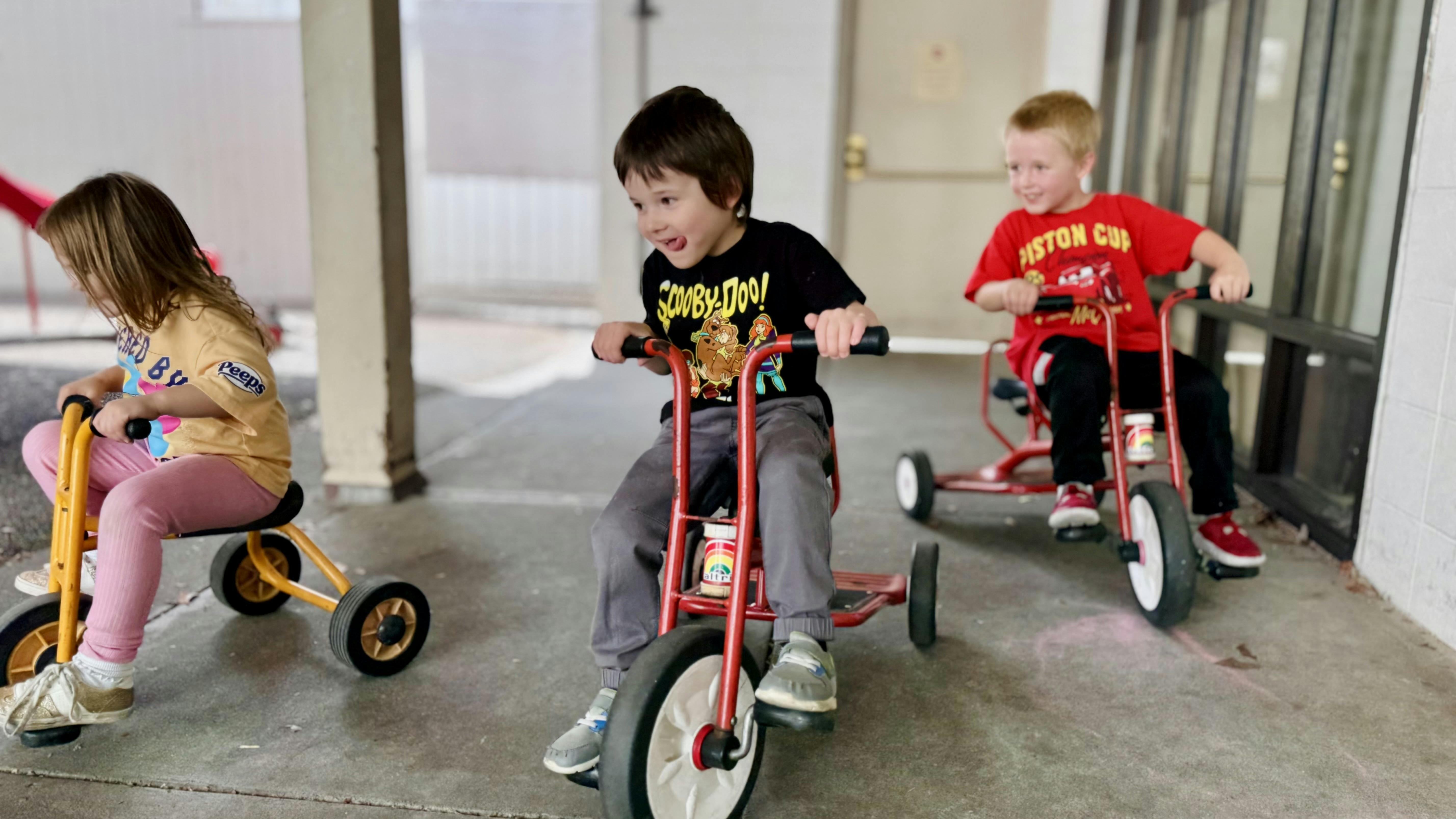 Three children riding tricycles outdoors