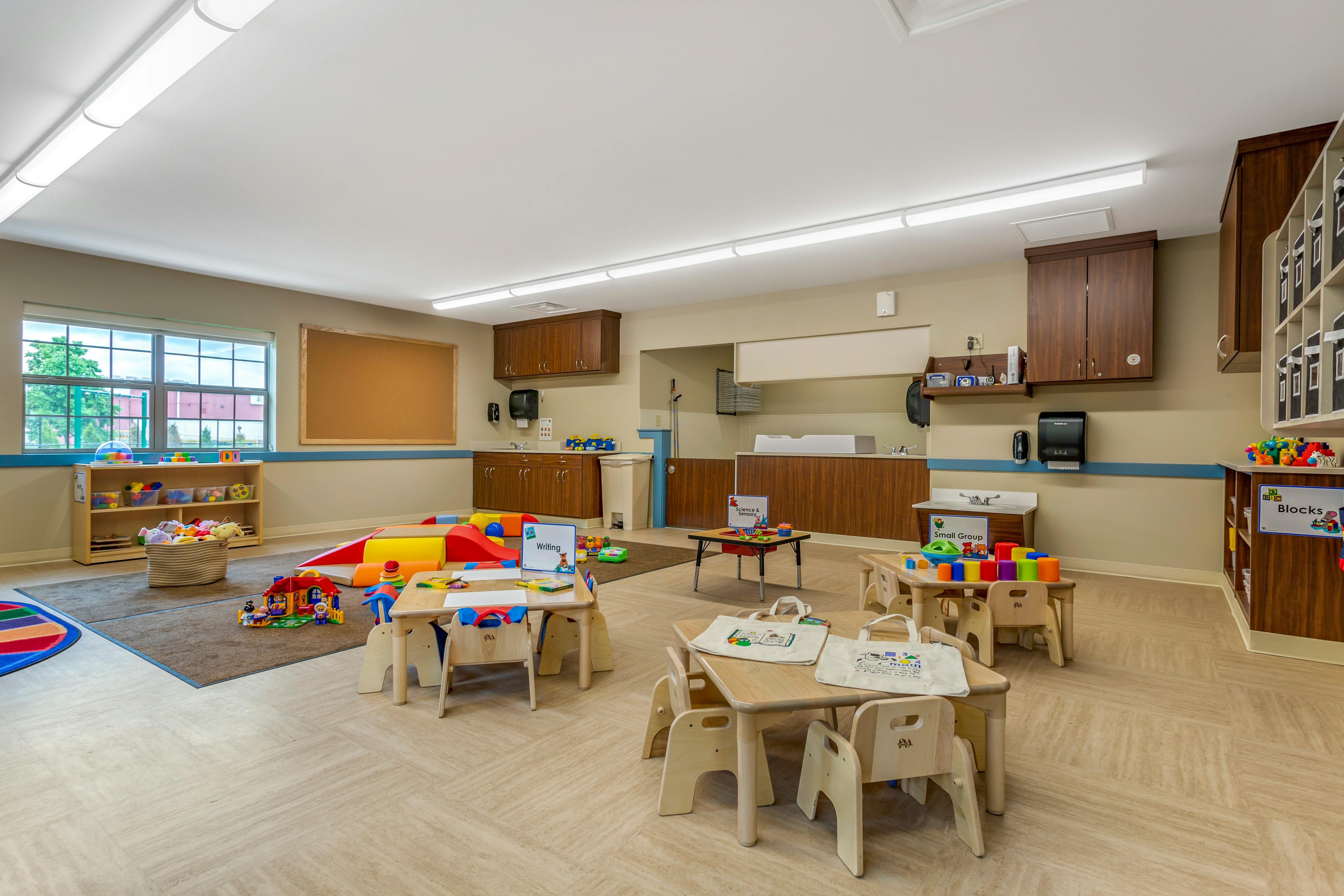 Classroom with small tables and chairs, play mats, and learning stations