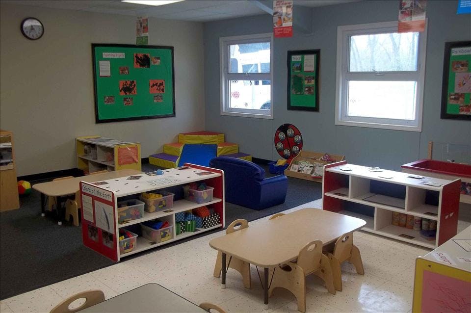 A classroom with small tables and chairs, shelves with toys, and colorful play mats