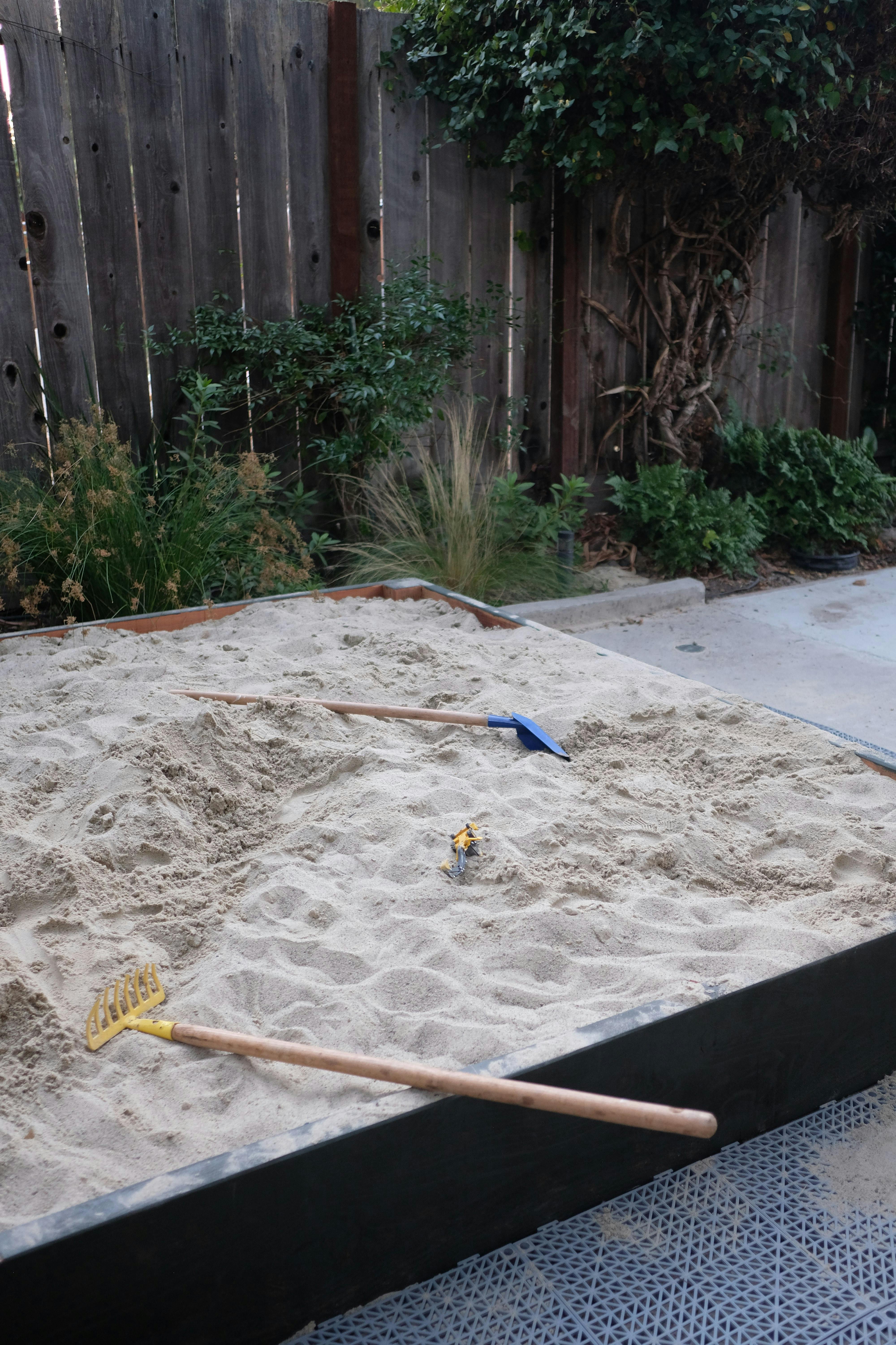 Sandbox with a blue shovel and yellow rake