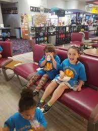 Two children sitting on a bench, one drinking and one eating