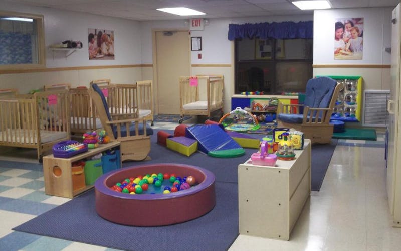 Cribs, play mats, toys, and a ball pit in a daycare classroom