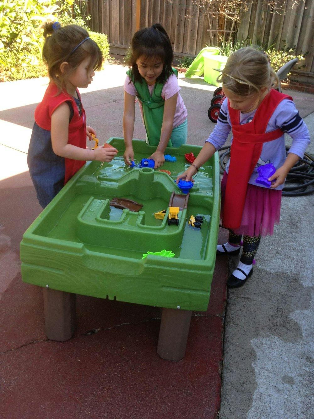 Three children playing with a green water table