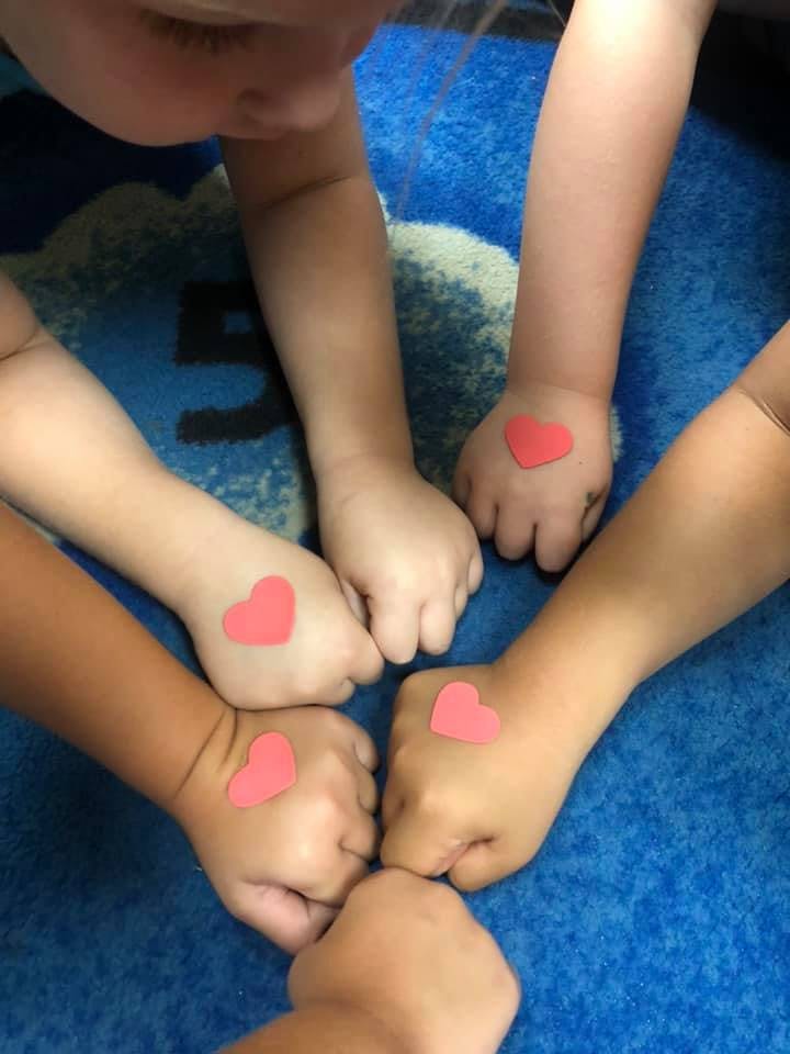 Multiple children's hands with heart stickers on them
