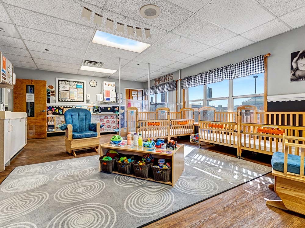 Infant room with multiple cribs, a blue rocking chair, and a rug with circle patterns