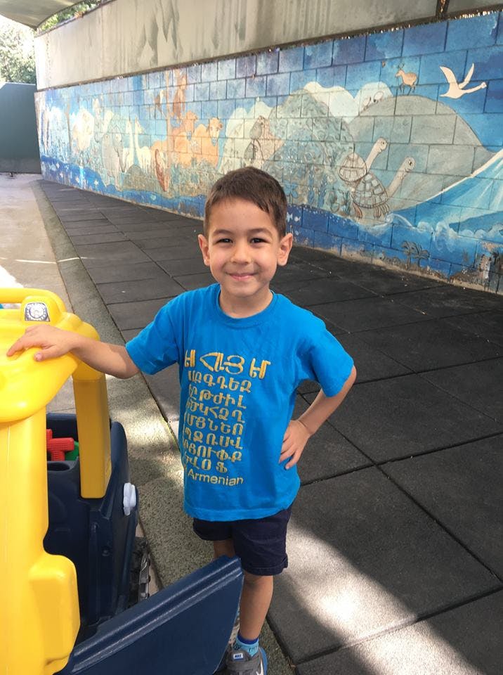 Child in a blue shirt with text, standing next to a yellow toy