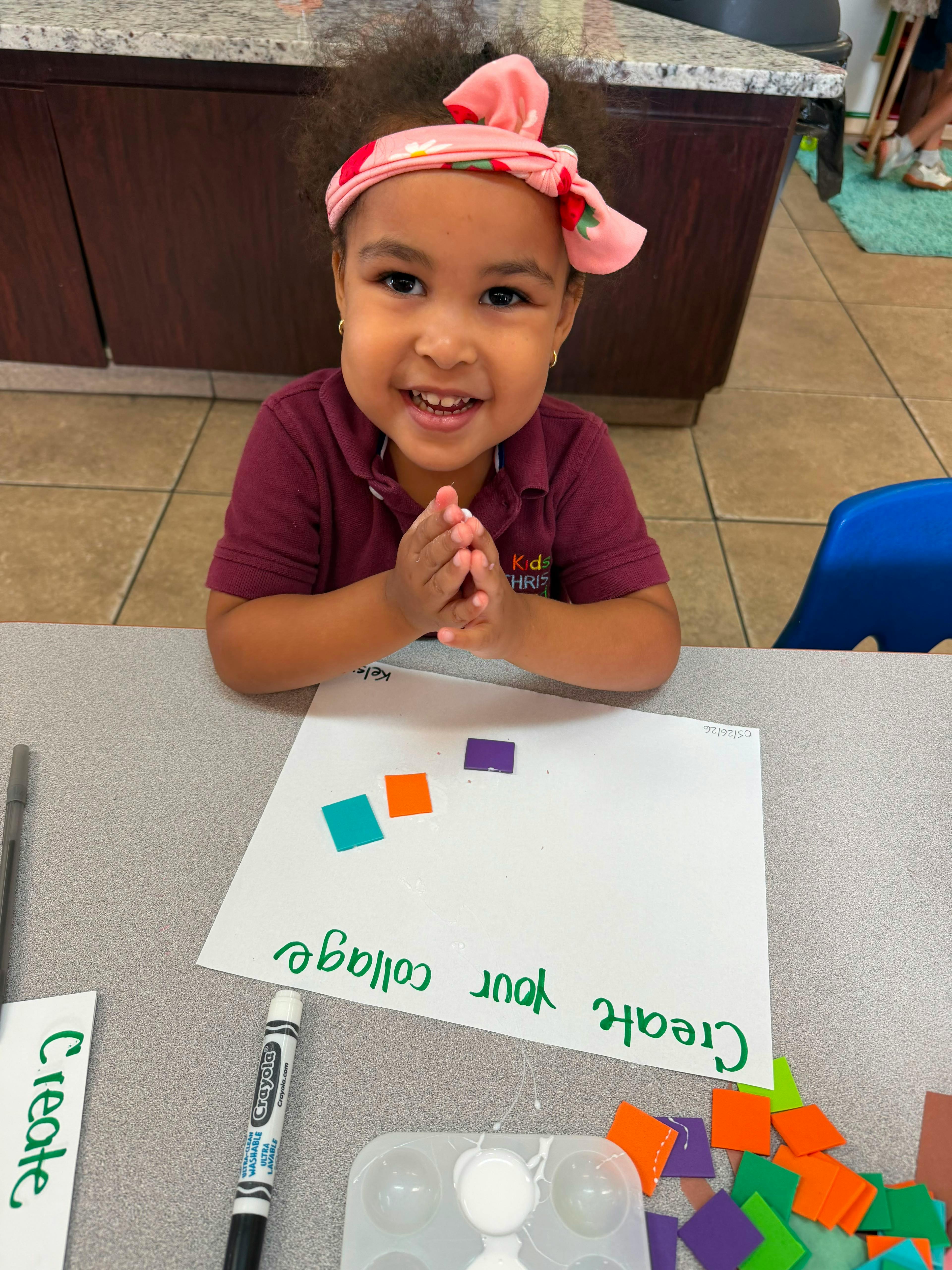 Child sitting at a table working on a collage with paper squares
