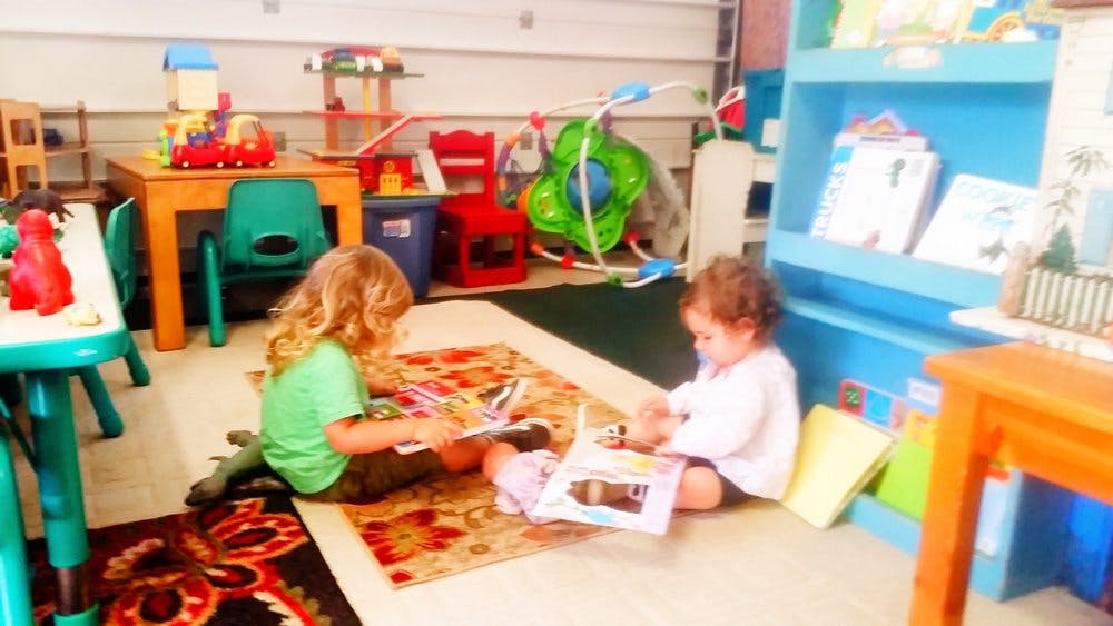 Two children sitting on rugs and looking at books in a playroom