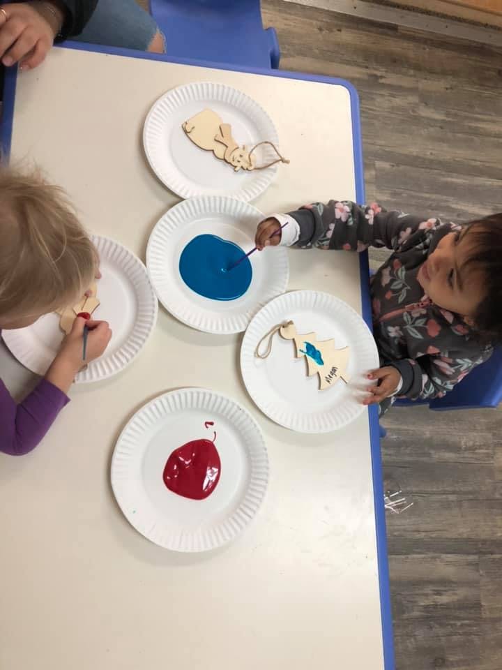 Two children painting wooden cutouts at a table