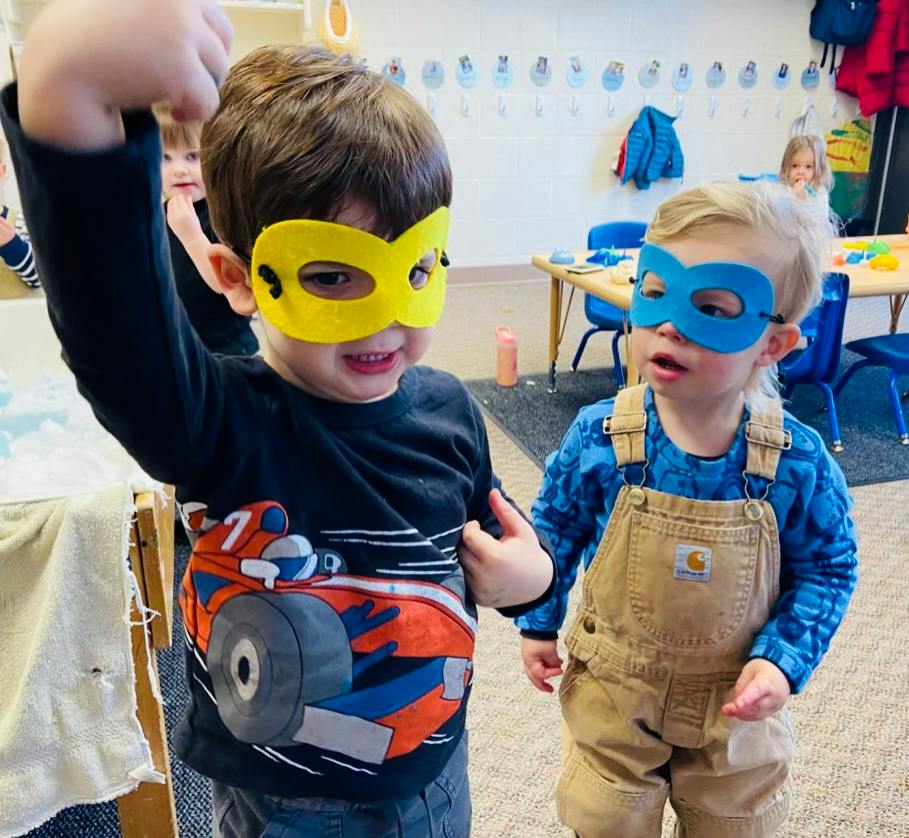 Two children wearing superhero masks in a classroom