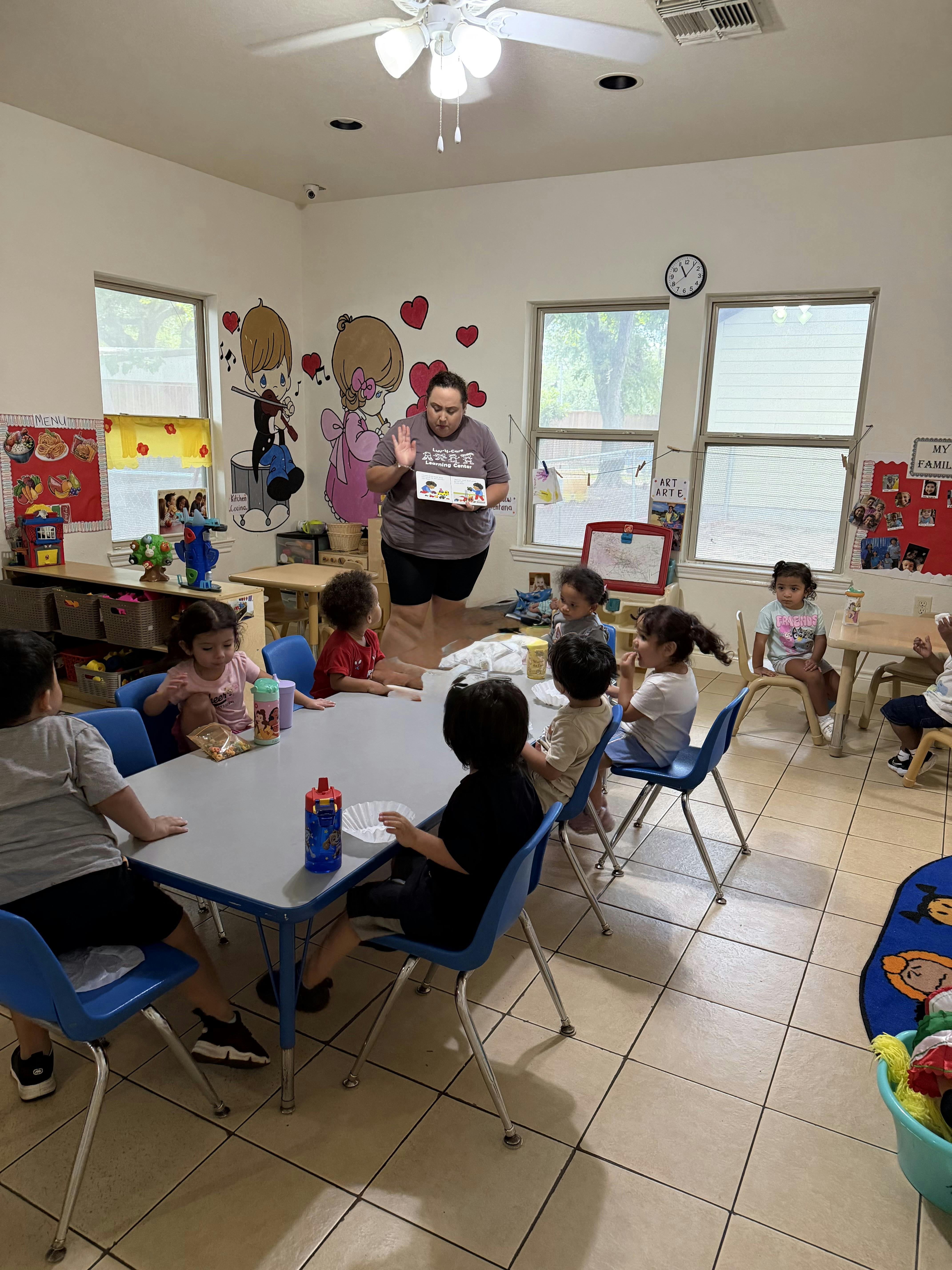 Adult reading a book to a group of children at a table in a classroom