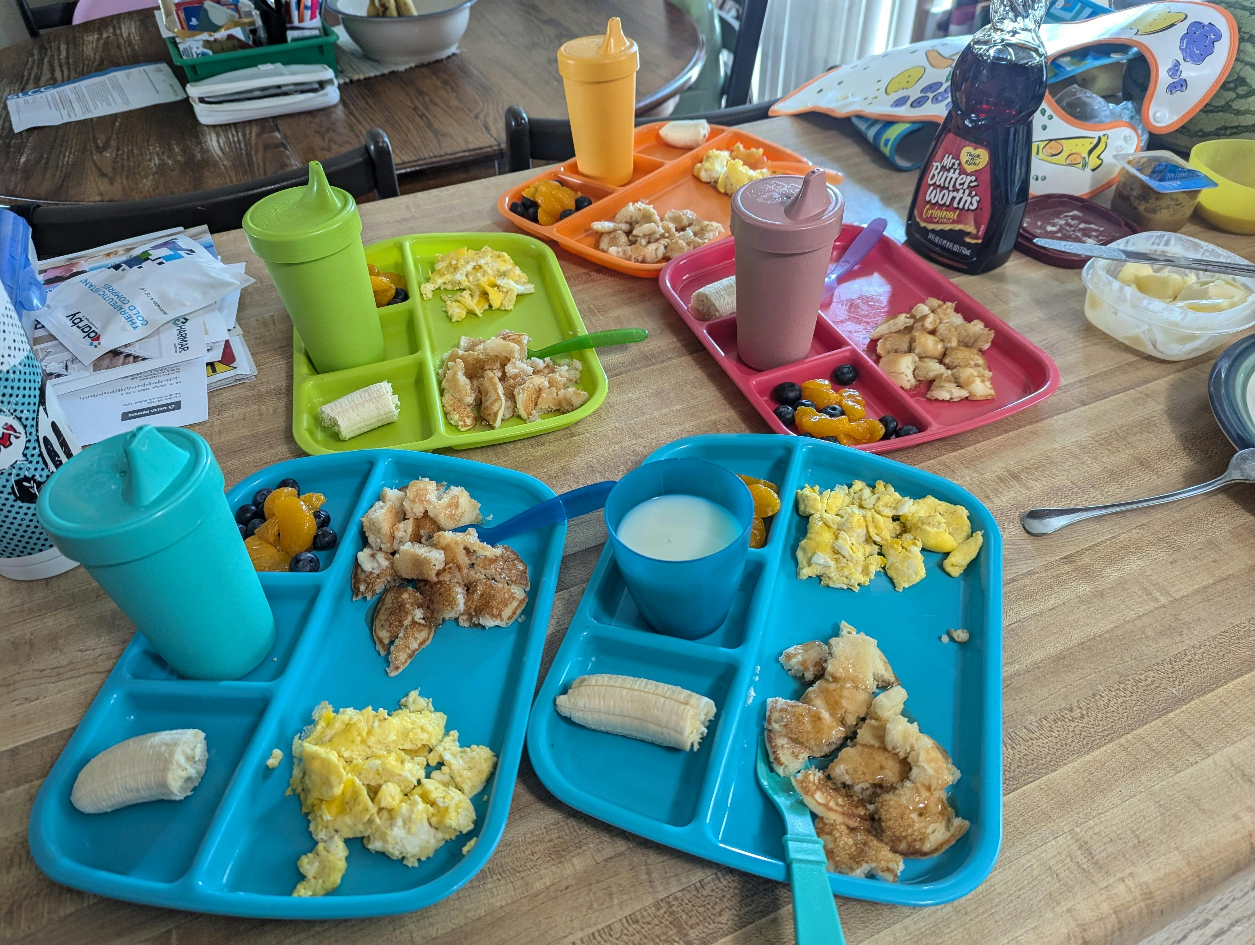 Multiple children's plates with scrambled eggs, fruit, and pancakes