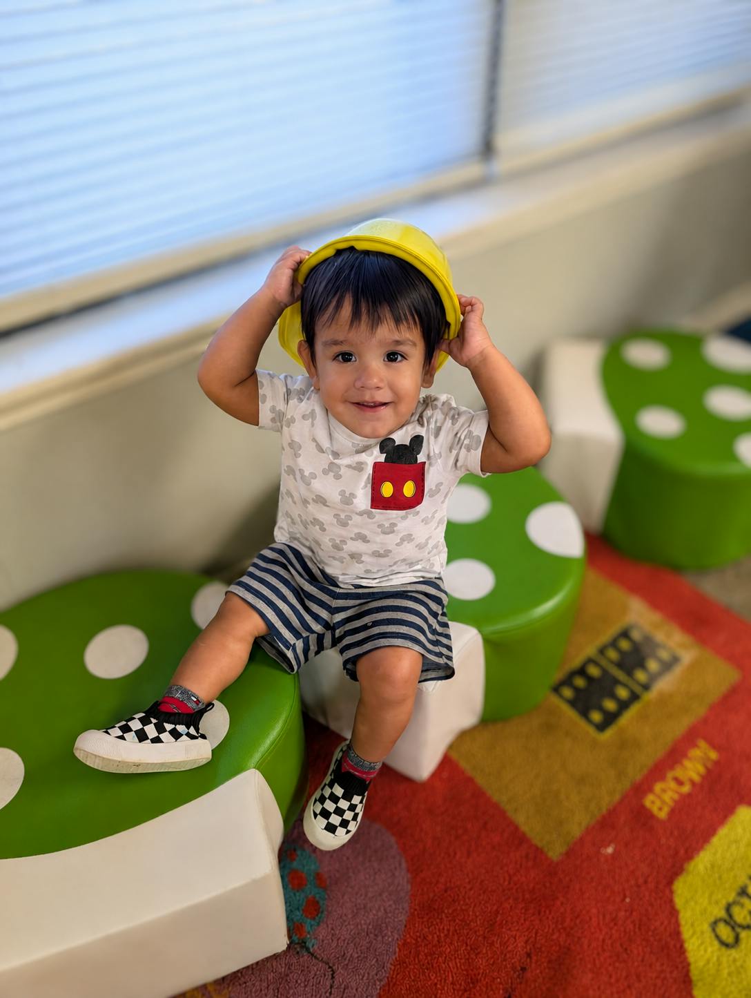 Child wearing a toy hard hat while sitting on a mushroom-shaped seat