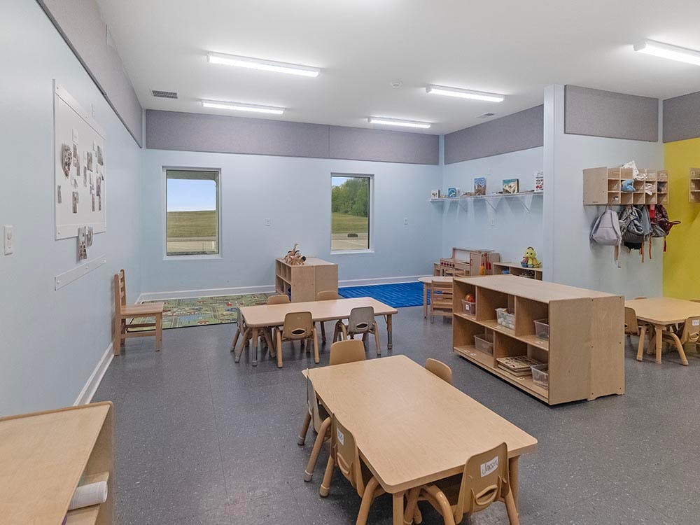 Classroom with small tables and chairs, storage shelves, and windows