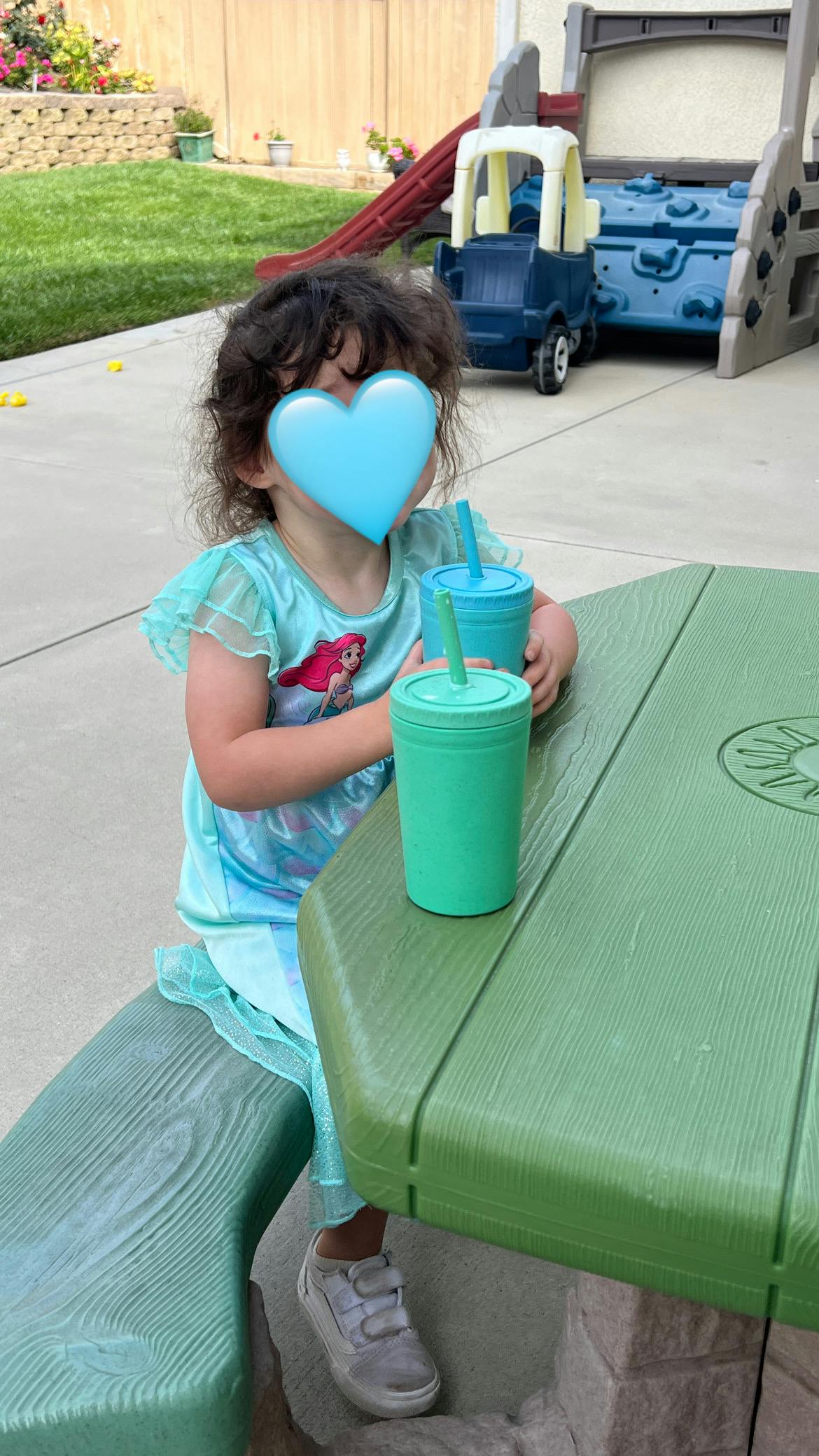 Child sitting at a green picnic table with two cups