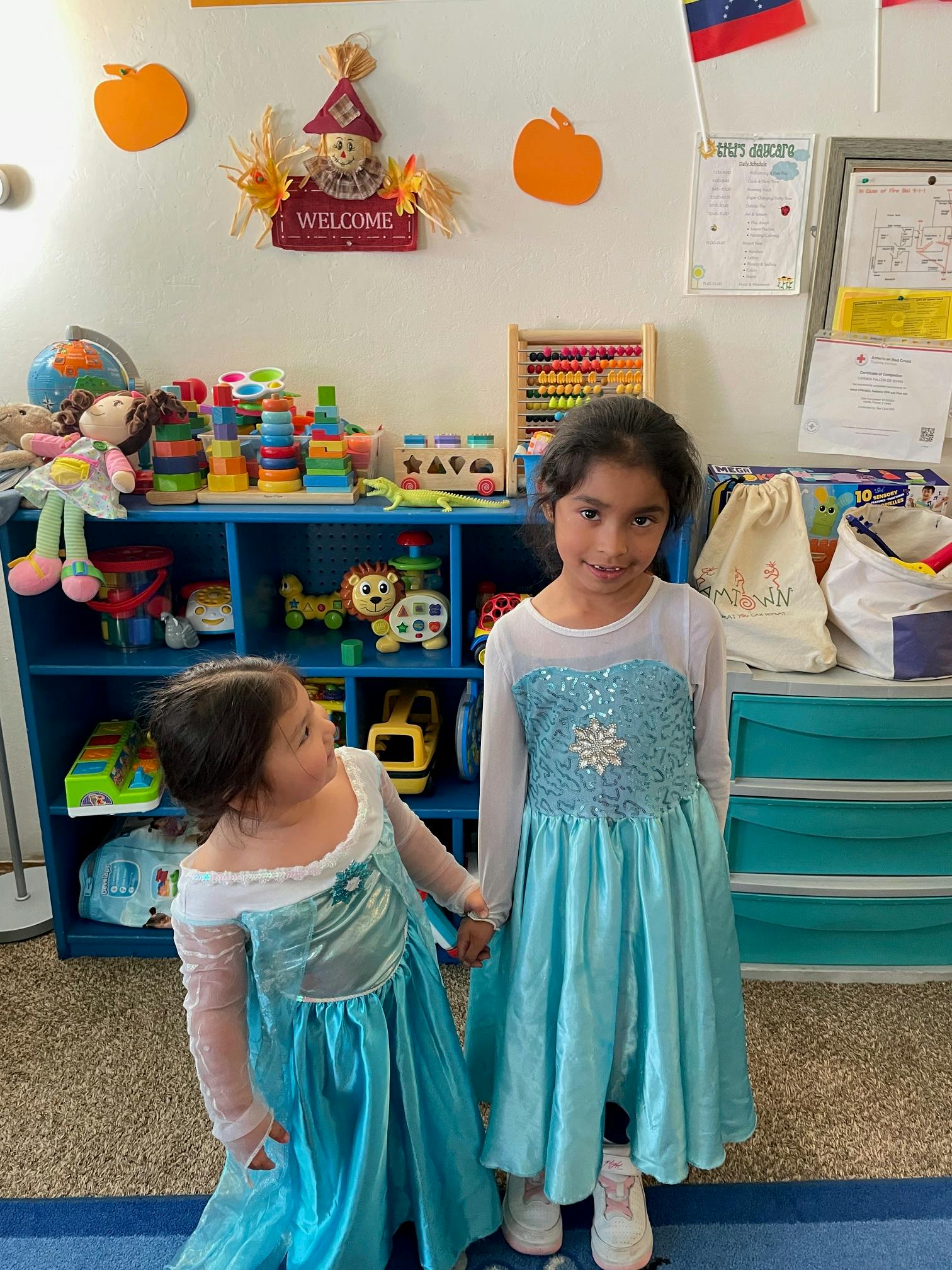 Two children in blue dresses standing in a room with toys