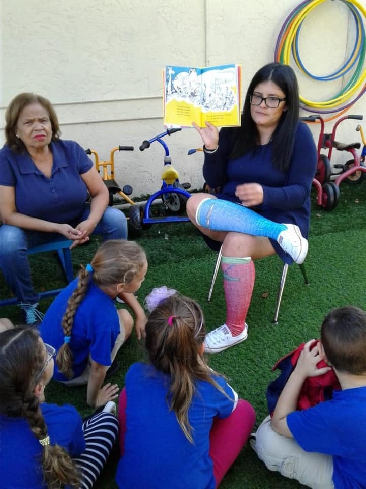 Person reading a book to children and an adult sitting on grass