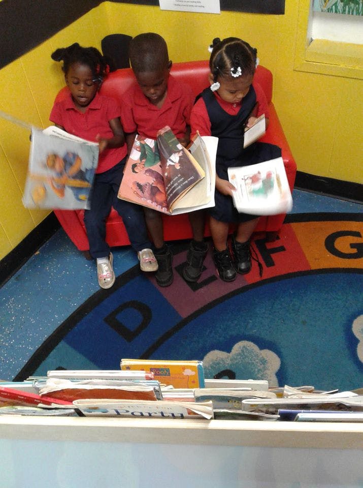 Three children sitting on a red couch reading books