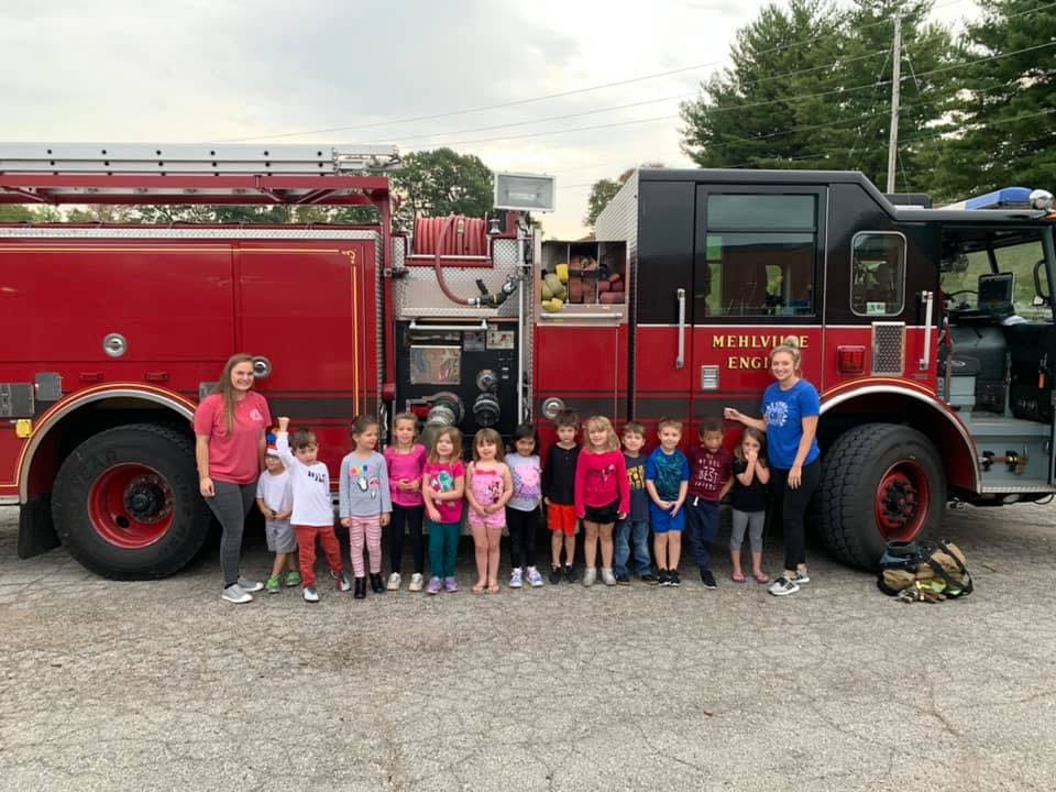 Two adults and a group of children standing in front of a fire truck
