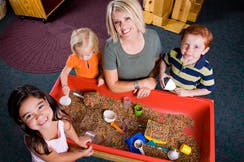 Adult and three children playing in a sand table