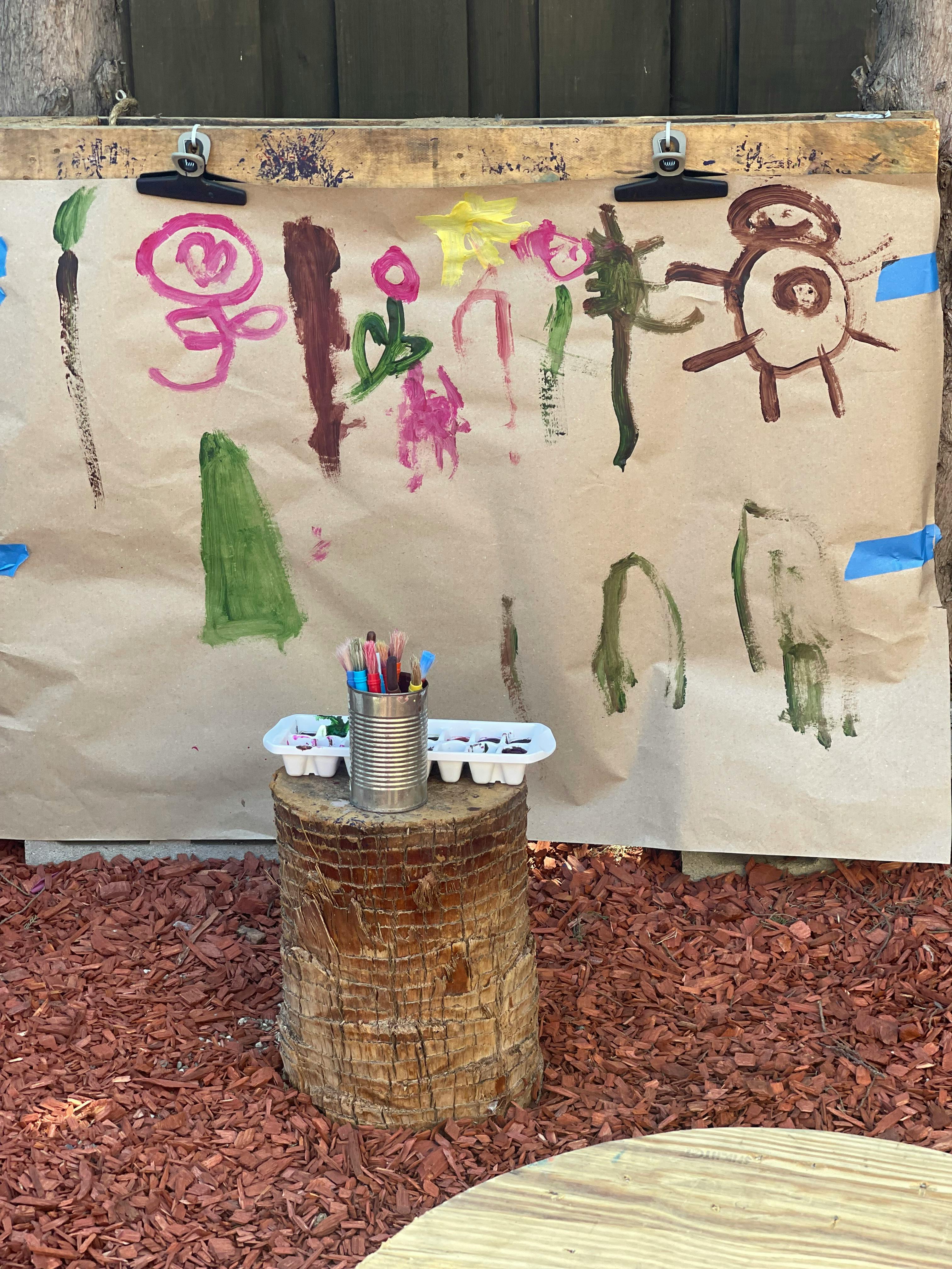 Child's painting on paper with paintbrushes in a can on a tree stump