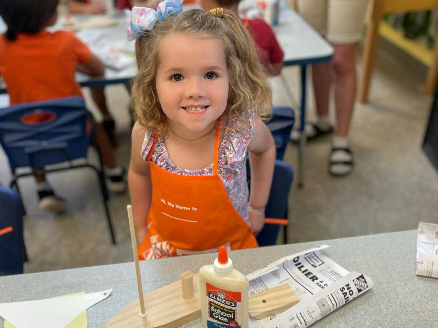 Child in an orange apron sitting at a table with craft supplies