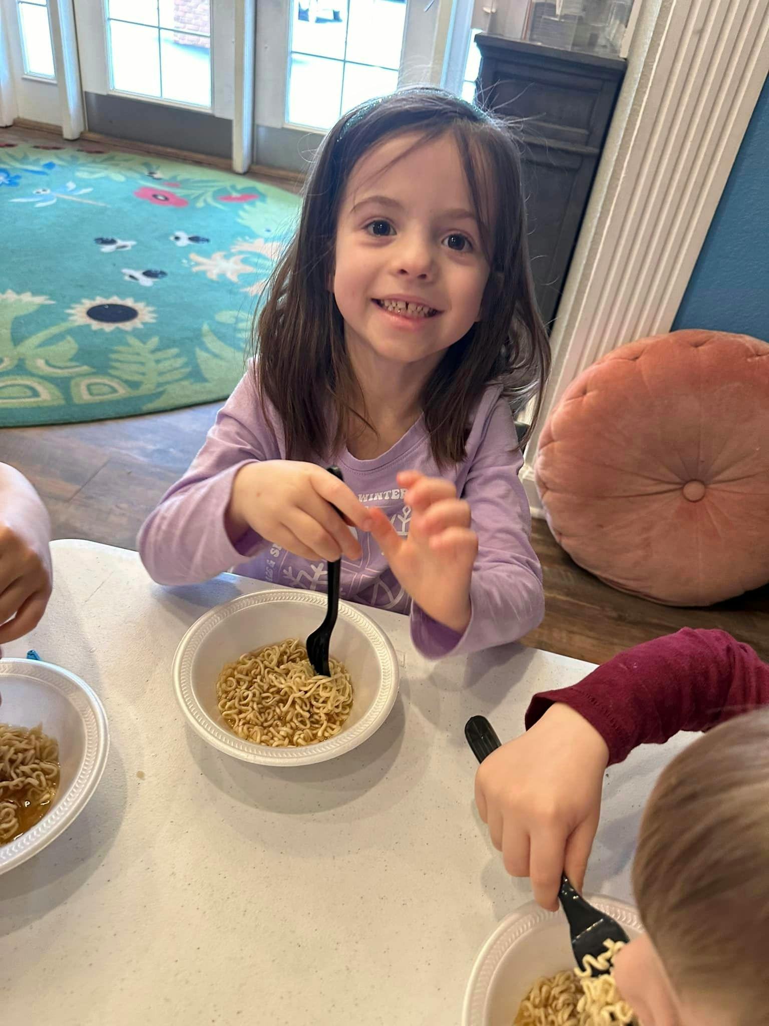 Child eating noodles with a fork at a table